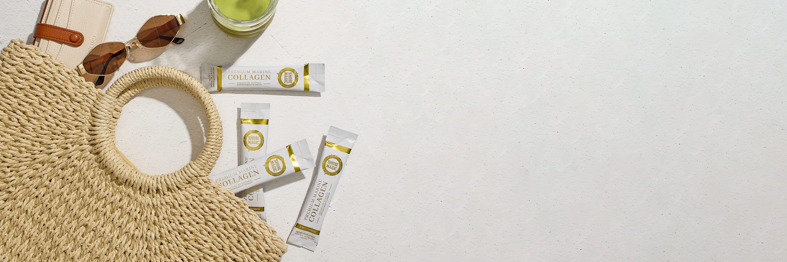 Shore Magic collagen packets spilling out from a beach bag with sunglass and glass of matcha