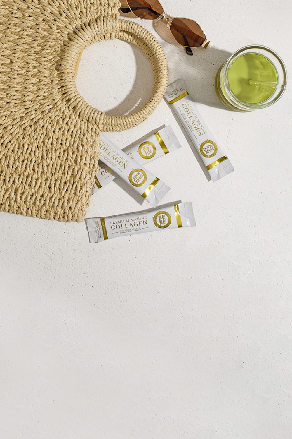 Shore Magic collagen packets spilling out from a beach bag with sunglass and glass of matcha