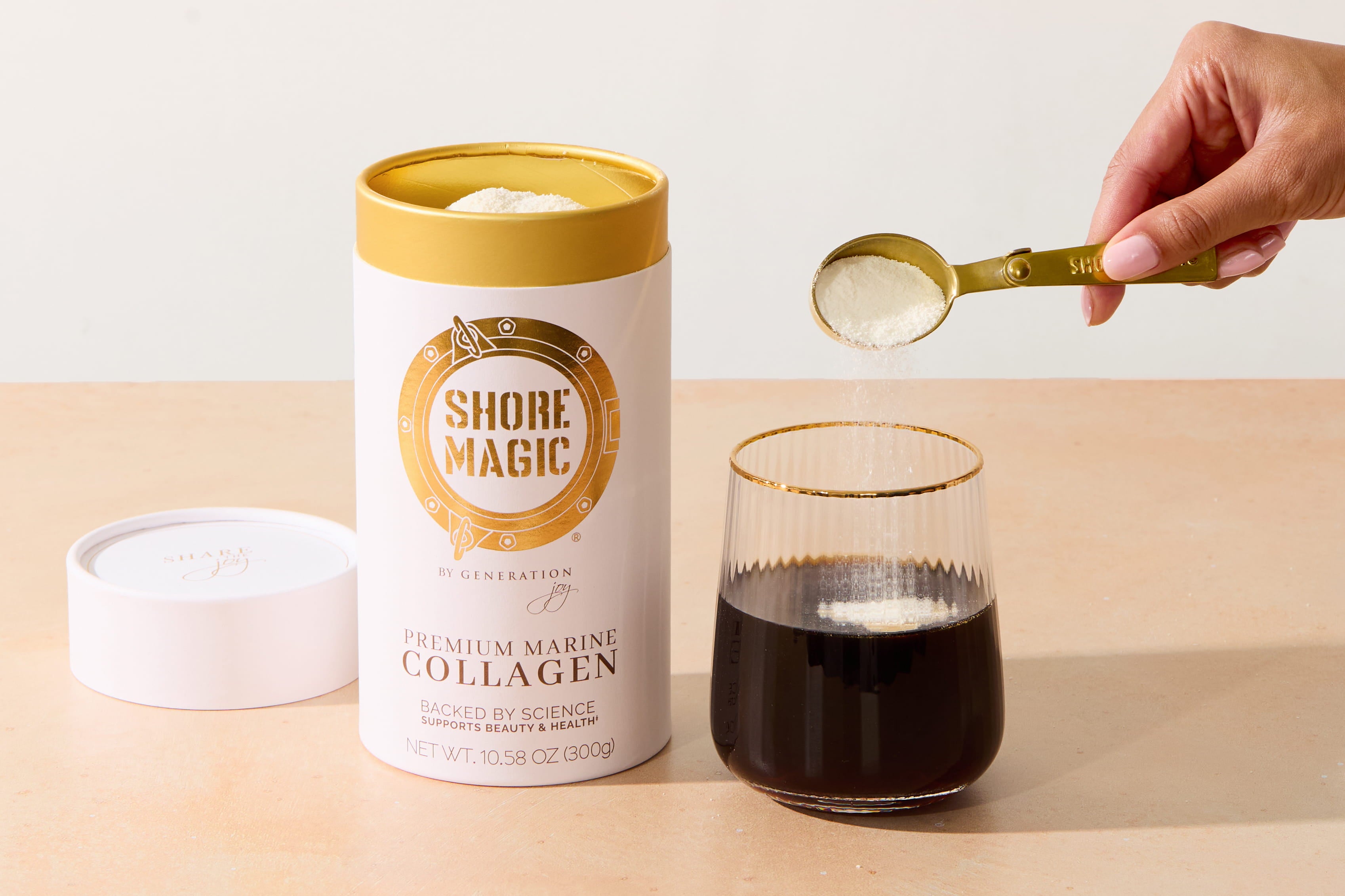 Woman holding a gold spoon with collagen powder being poured into a glass cup of coffee, next to 30 day supply of Shore Magic 30 day supply